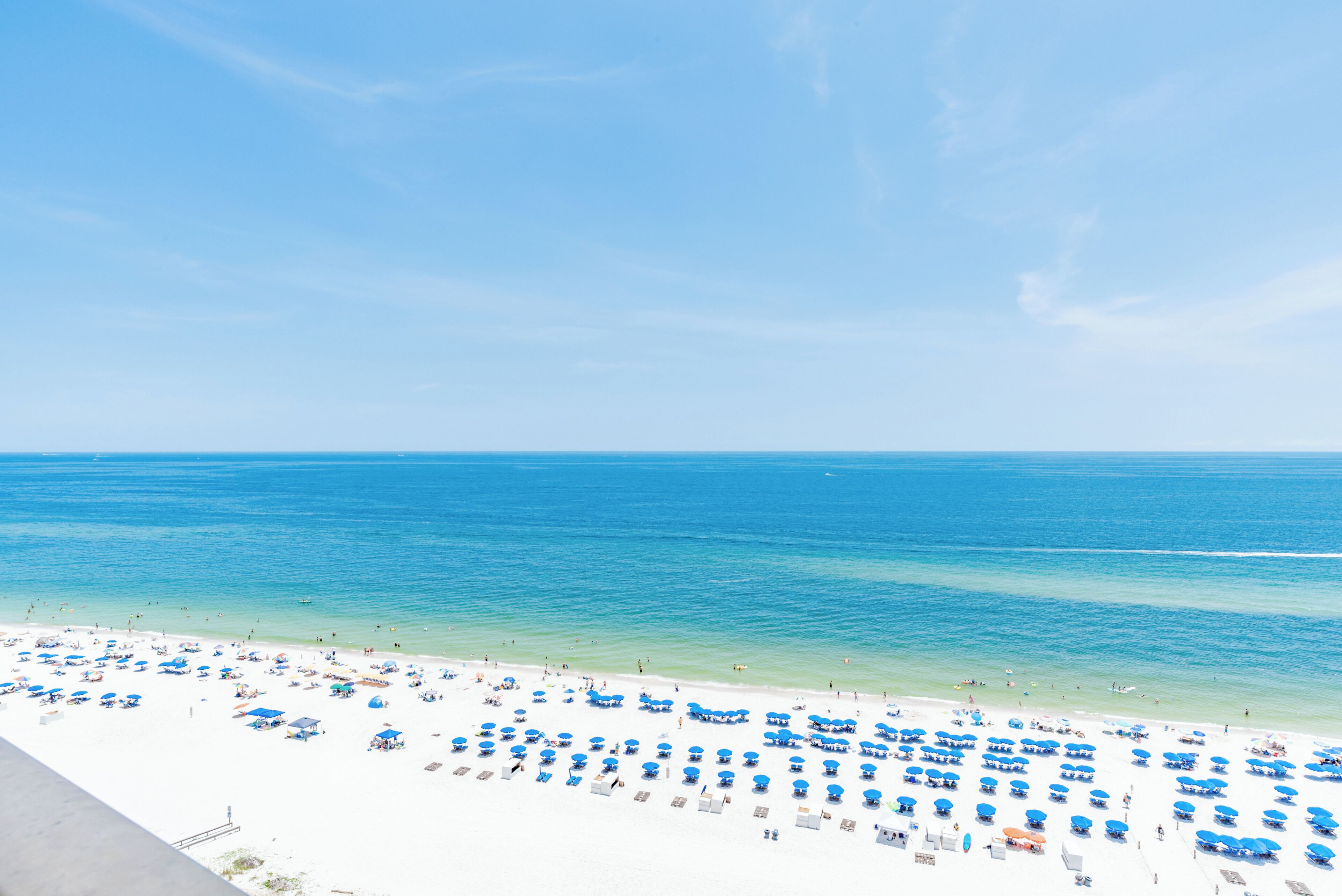 A beach with numerous blue umbrellas and white sand.