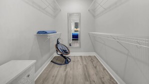 Un couloir étroit aux murs blancs et au plancher en bois, comprenant un banc blanc, une chaise et deux étagères blanches.