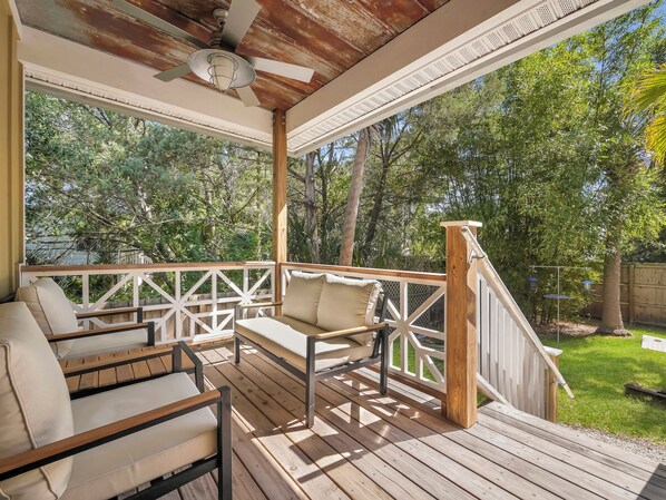 A covered outdoor seating area with wooden furniture and a ceiling fan.