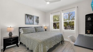 Une chambre à coucher avec un lit, des tables de chevet, un bureau et une fenêtre avec des stores.