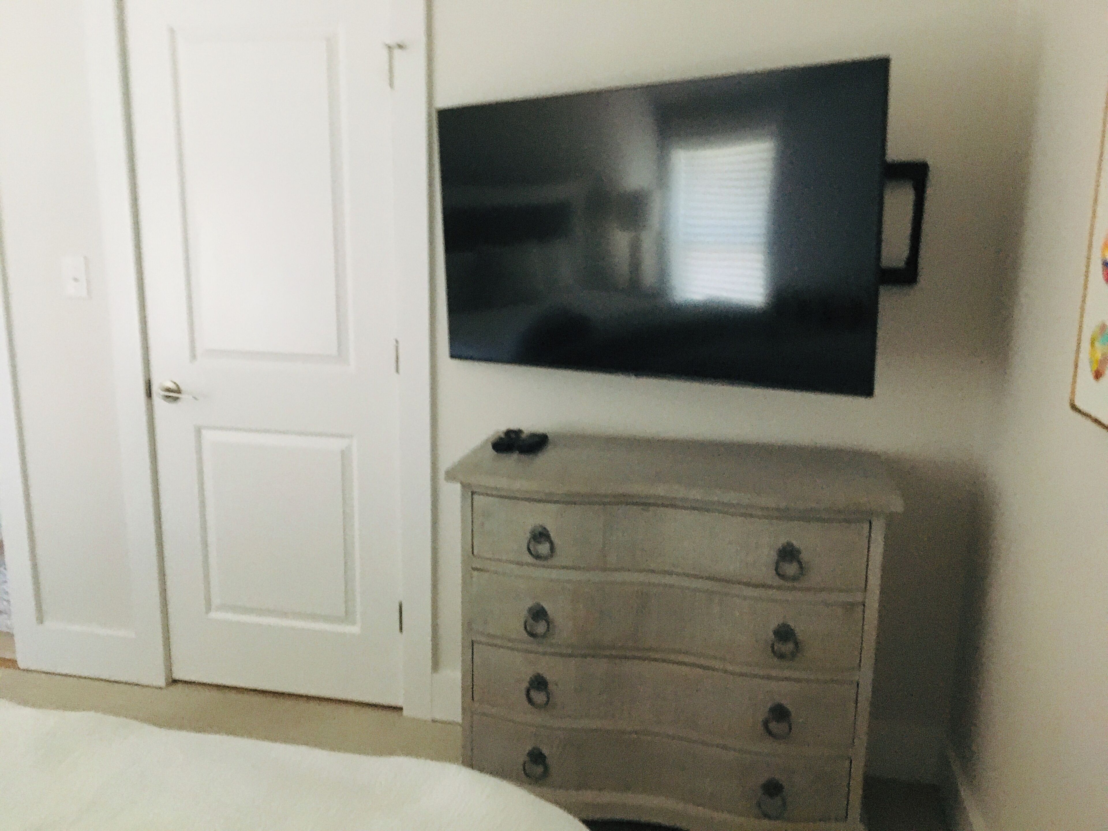 A room with a white door, a flat-screen TV mounted on the wall, and a wooden dresser with drawers.