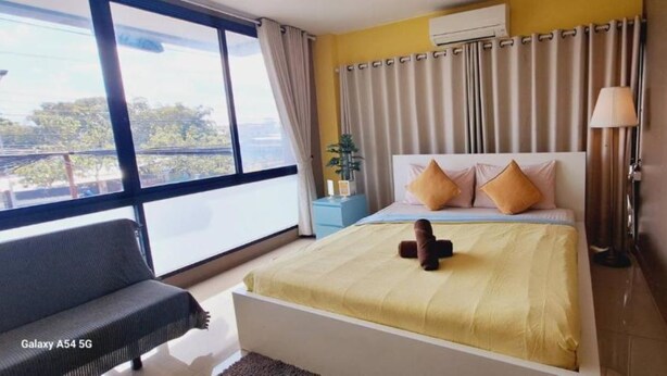 A modern hotel room with a large bed, a bedside table, a lamp, and a view of the city through large windows.