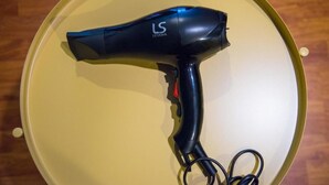 A black hair dryer with a cord on a yellow surface.