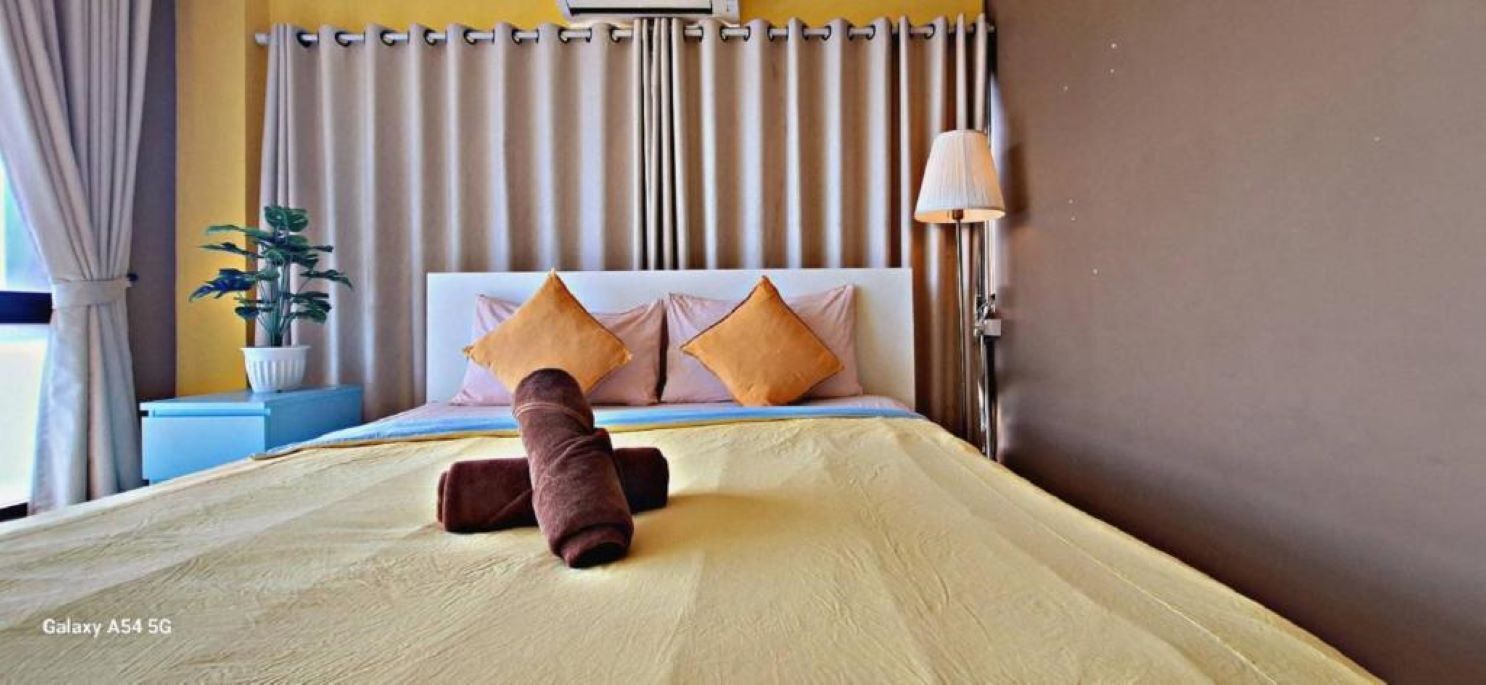 A hotel room with a bed, pillows, a lamp, and a plant.