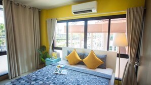 A hotel room with a bed, a window with curtains, a bedside table with a lamp, and a view of the outside.