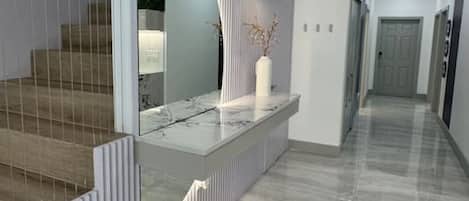 Un interior moderno con encimera de mármol, un florero blanco y un espejo curvo.