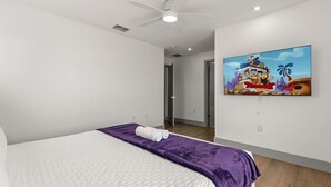 Habitación de hotel con cama, ventilador de techo, un cuadro en la pared y una puerta que da a otra habitación.