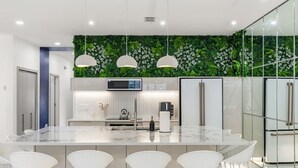 Una cocina moderna con una isla grande, taburetes de bar blancos, un microondas y un refrigerador.