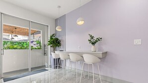 Una cocina moderna con puerta de cristal que da a un balcón, taburetes de bar blancos e iluminación colgante.