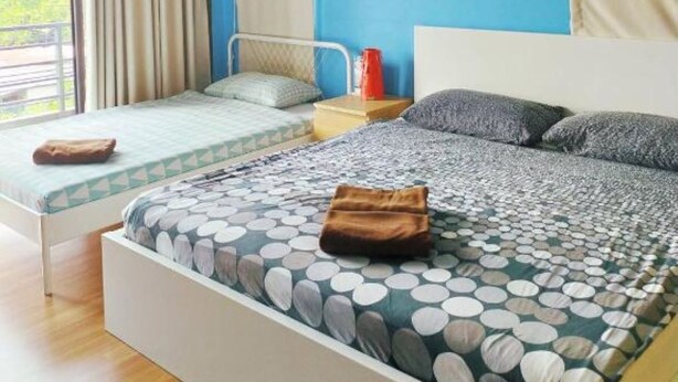 Un dormitorio con dos camas, una pared azul, una lámpara en el techo y una ventana con cortinas.