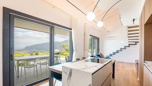 A modern kitchen with a marble island, a dining area with a table and chairs, and a staircase leading to an upper level. - Villa Melodia - Scopello (Scopello)
