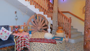A room with a large wooden wheel, a staircase with wooden balusters, a patterned rug, and a blue-tiled floor.