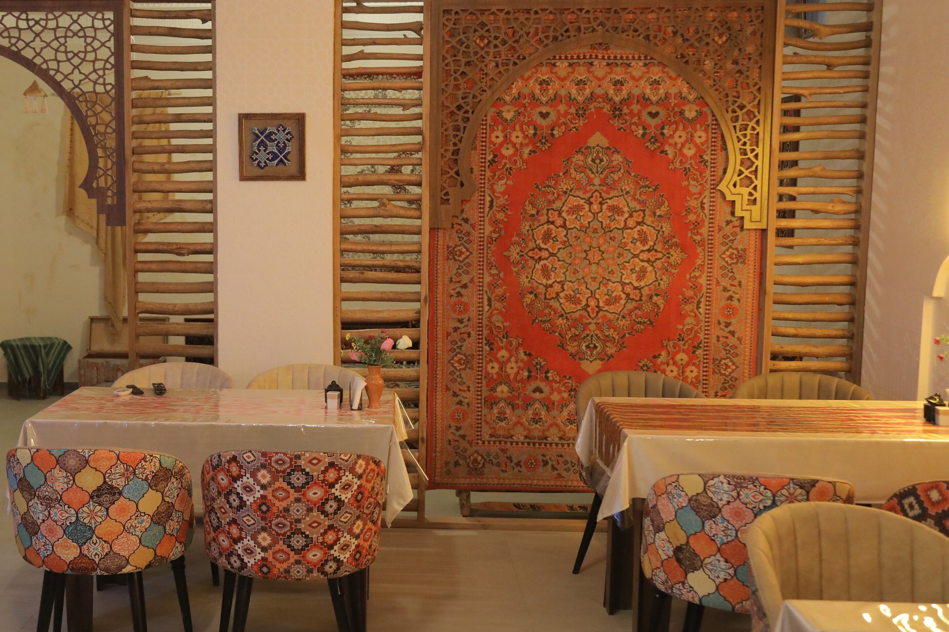 A dining area with a table set for four, surrounded by patterned chairs, a large ornate rug, and a wooden lattice partition.