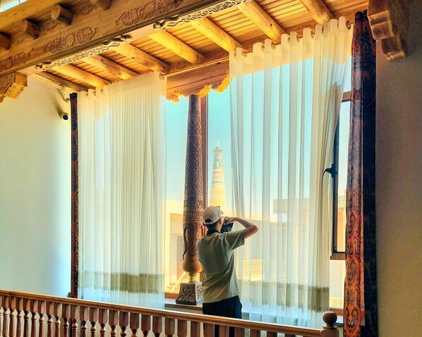 Una persona parada en un balcón con vistas a una torre a través de cortinas translúcidas.