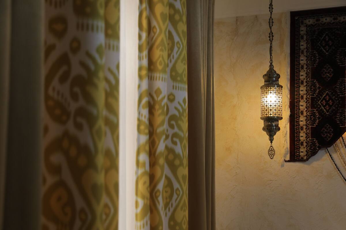 A room with patterned curtains, a hanging light fixture, and a wall with a decorative rug.