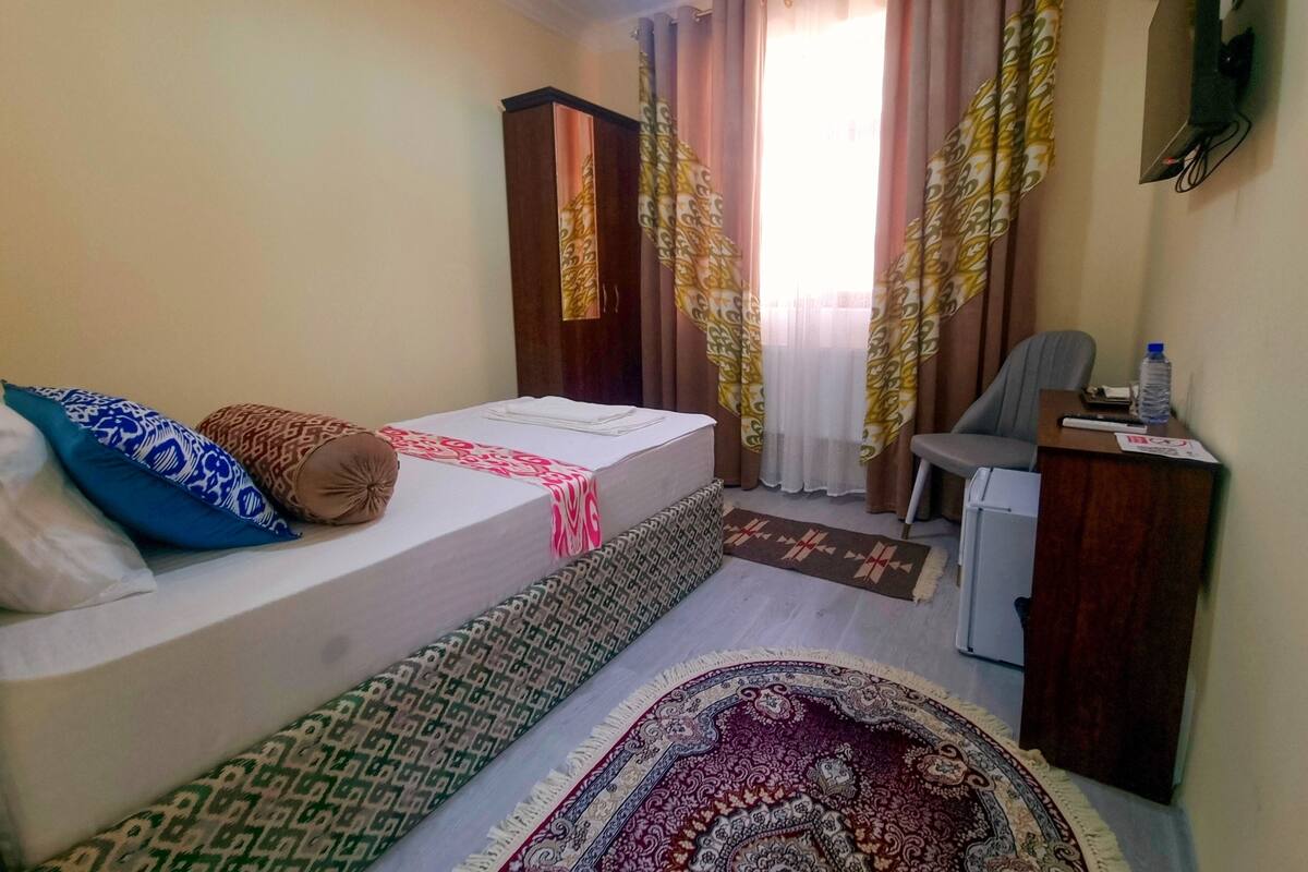 A hotel room with a bed, a desk, a chair, a wardrobe, and a television.