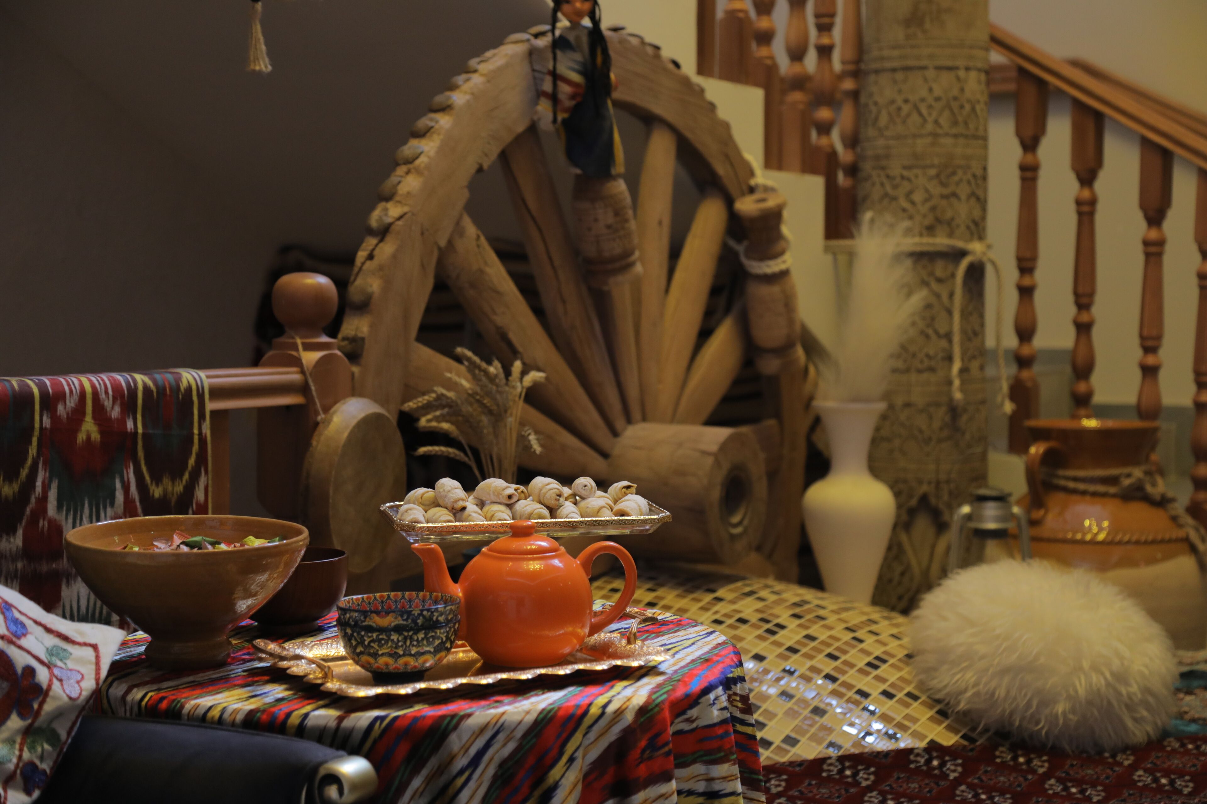 Une scène traditionnelle avec une roue en bois, une théière et un plateau de pâtisseries posés sur une nappe à motifs.