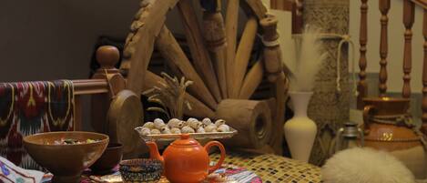 A traditional setting with a wooden wheel, a teapot, and a tray of pastries on a patterned tablecloth.