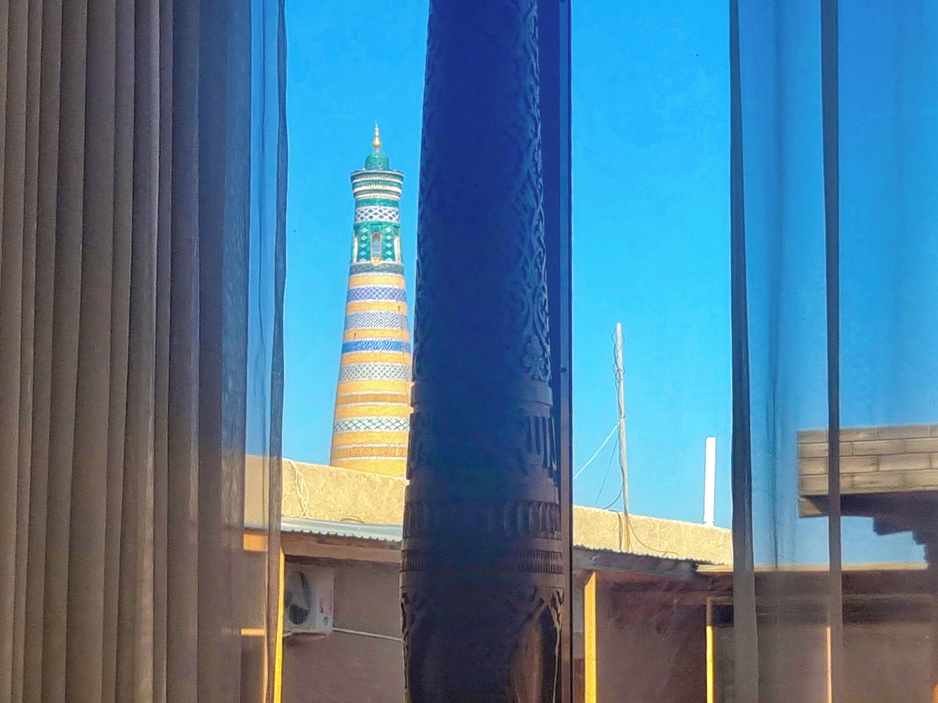 Vista di un minareto con decorazioni elaborate e una cupola, vista attraverso persiane.