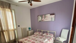 Een slaapkamer met een bed, een stoel, een plafondventilator, een radiator en een raam met gordijnen.