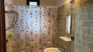 Een badkamer met een douchegordijn met cactussen en bloemen, een wastafel op een voetstuk, een handdoekhouder en een spiegel aan de muur.