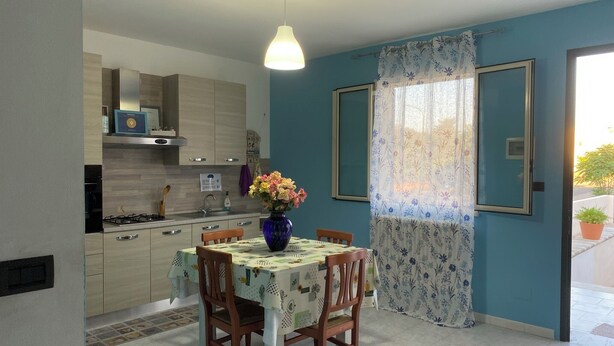 Een eetgedeelte met een tafel voor twee, een bloemenvaas en een keuken op de achtergrond.