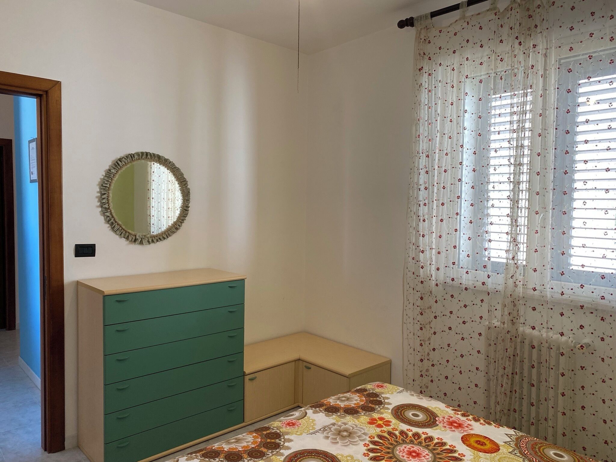 Un dormitorio con una cama, un tocador, un espejo y una ventana con cortinas florales.