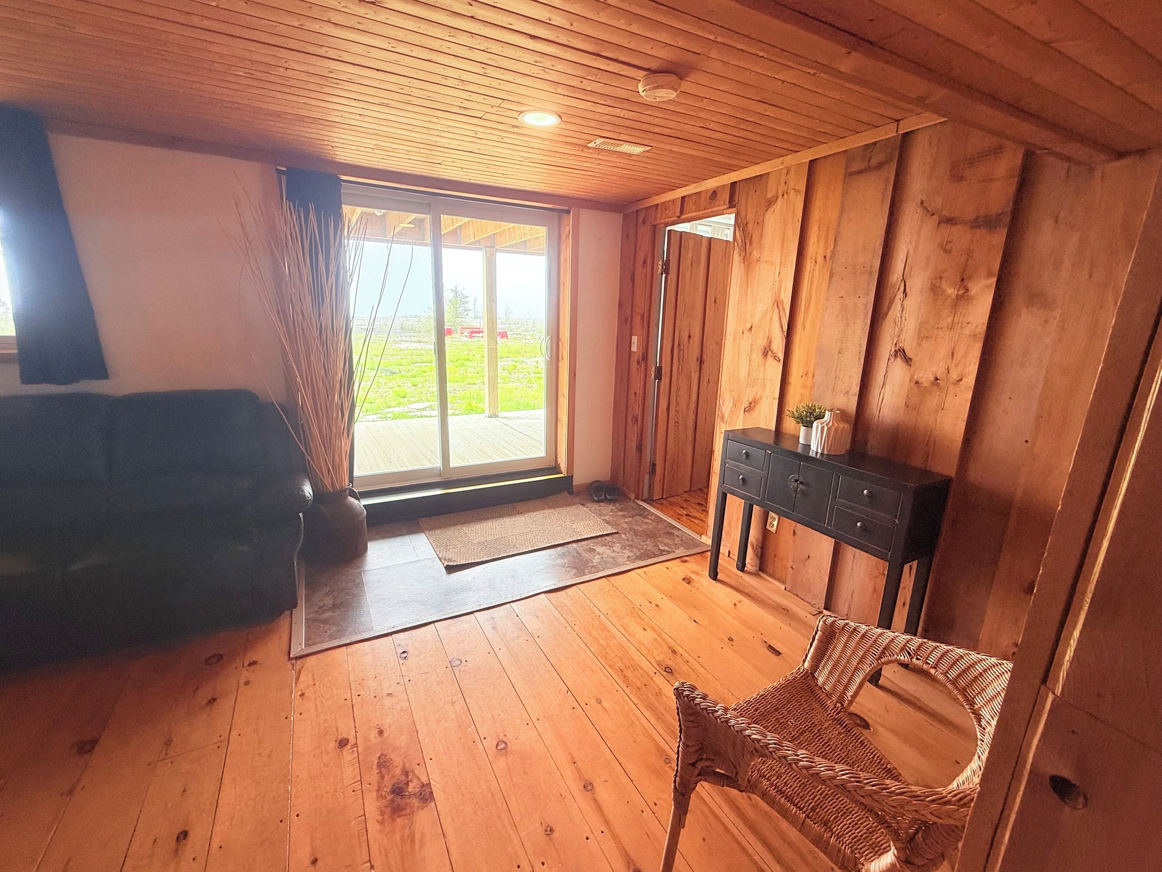 A room with wooden floors, a sliding glass door leading to an outdoor area, a wicker chair, and a dark-colored console table.