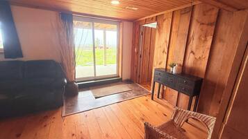 A room with wooden floors, a sliding glass door leading to an outdoor area, a wicker chair, and a dark-colored console table.