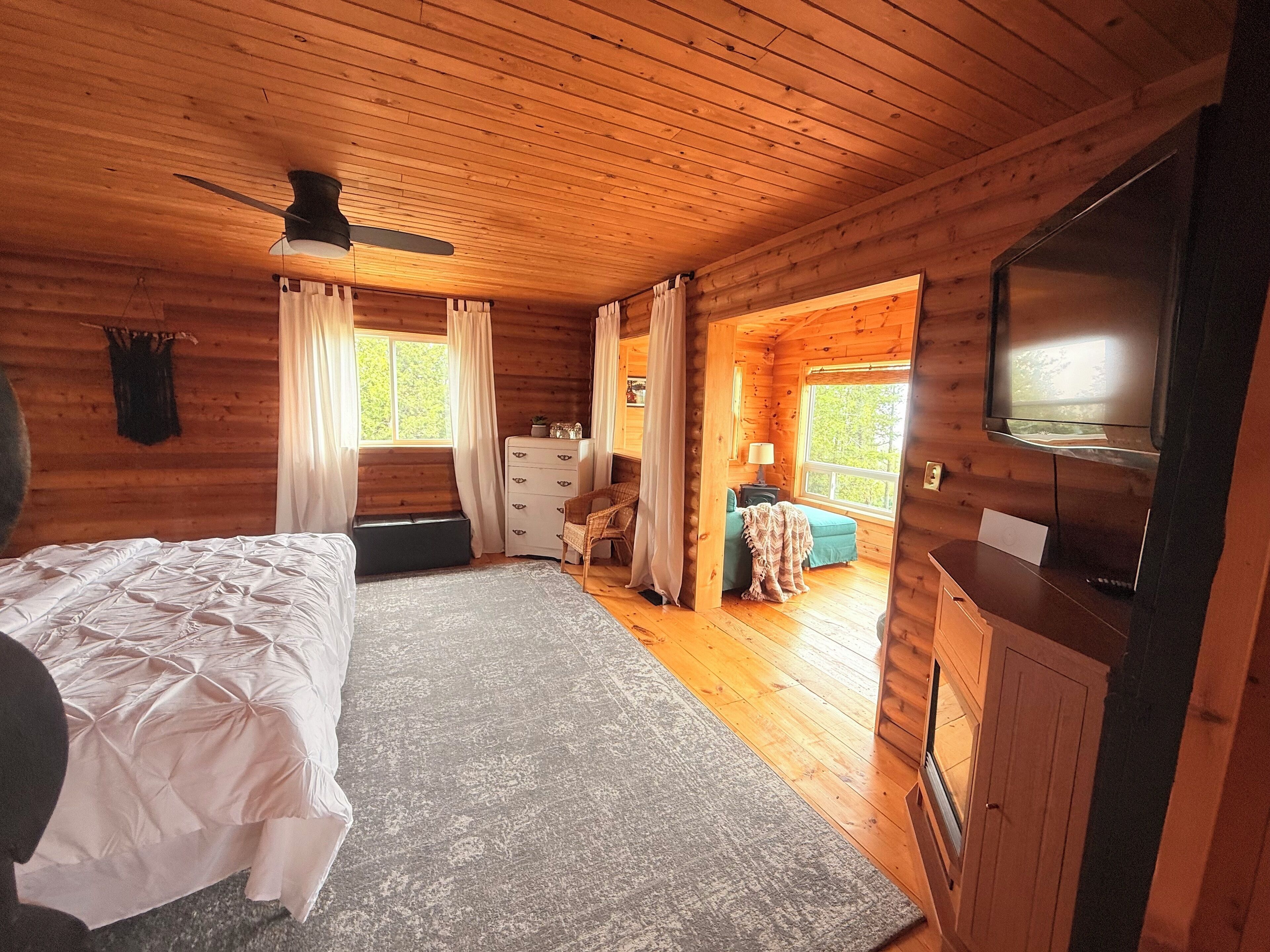 Une chambre rustique en bois, avec un lit, une commode, une télévision et une vue sur l’extérieur.