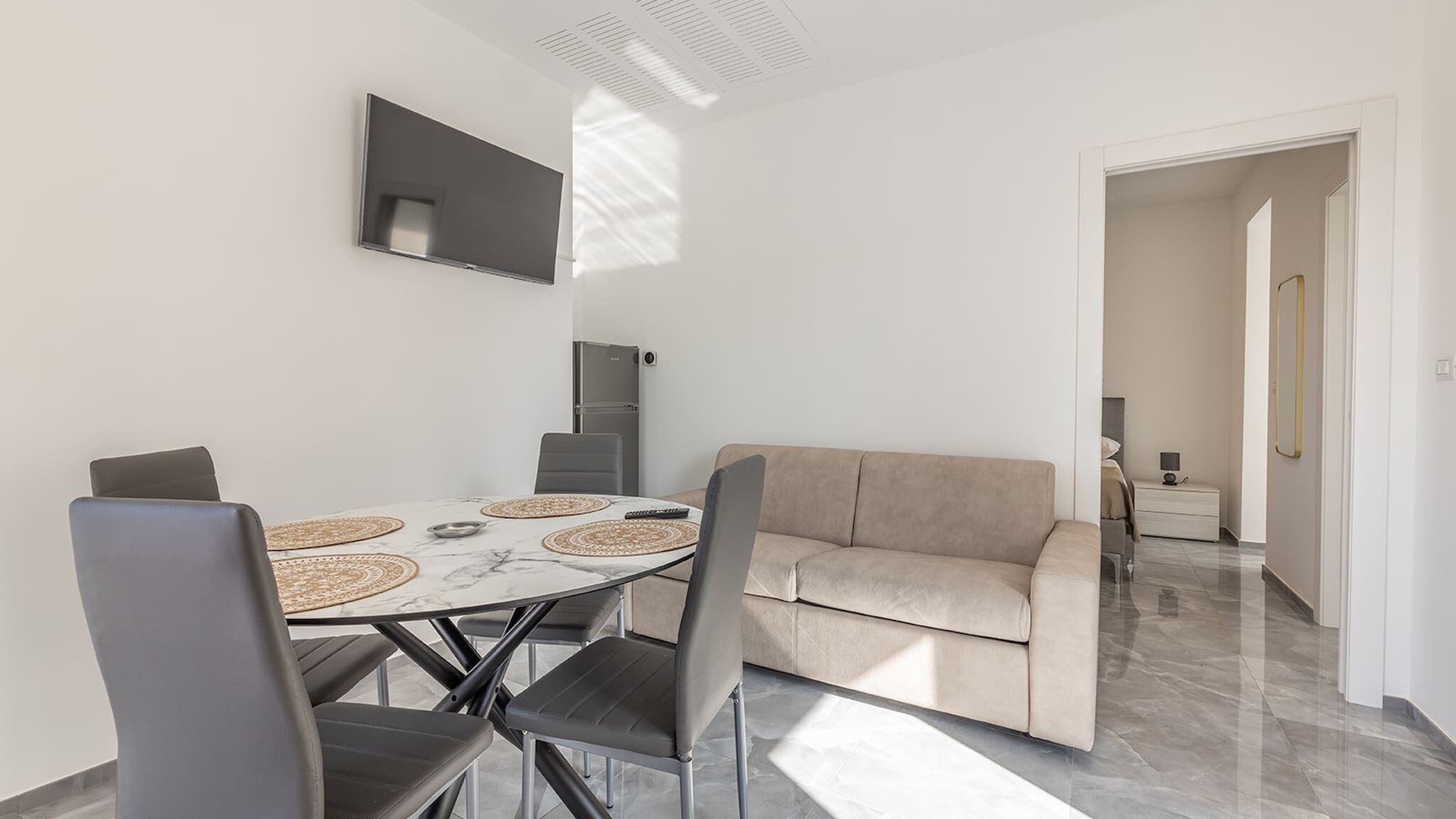 A modern living room with a round dining table, two sofas, and a flat-screen TV mounted on the wall.