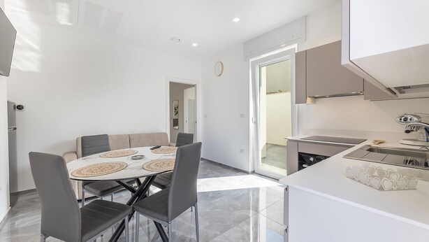Une cuisine moderne dotée d’un îlot central, d’un coin repas avec une table ronde et des chaises, et d’une grande fenêtre qui laisse entrer la lumière naturelle.