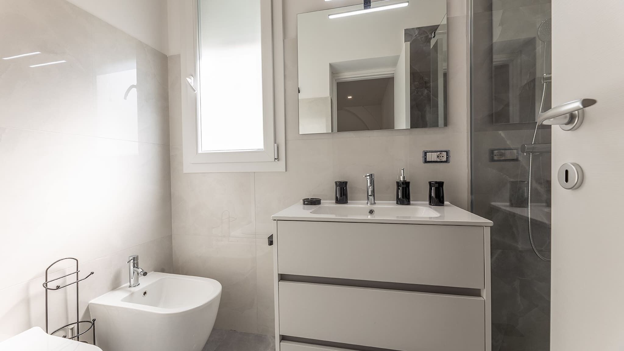 A modern bathroom with a white sink, a mirror, a shower, and a bidet.