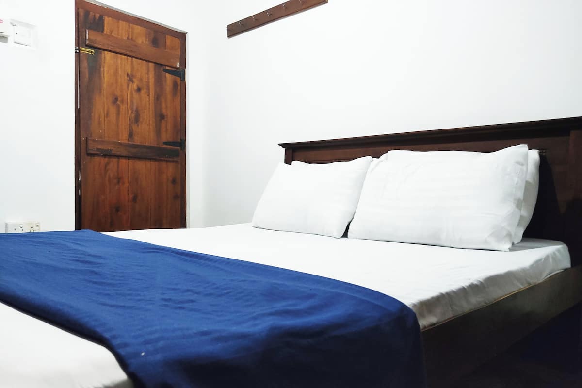 A bed with white bedding and a blue blanket, a wooden door, and a white wall.