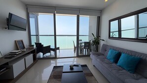 A modern living room with a sofa, coffee table, TV, and a balcony with a view of the sea. - 2704 Morros City - Spectacular beachfront apt (Cartagena de Indias)