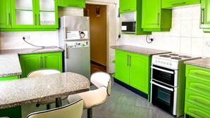 Une cuisine avec des meubles de rangement verts, un réfrigérateur, un four à micro-ondes, une cuisinière et un coin repas comprenant une table et des chaises.