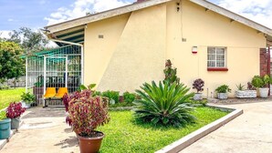 Un bâtiment à la façade jaune, doté d’une entrée abritée et d’un jardin où poussent différentes espèces de plantes.