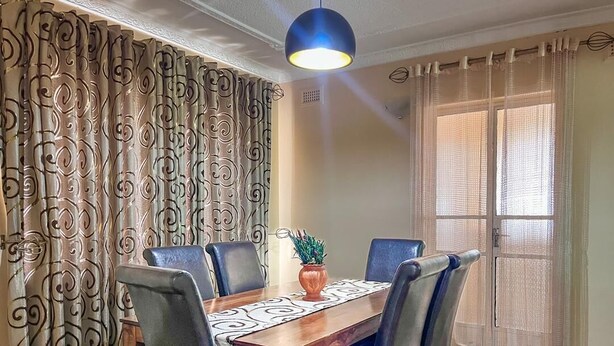 Un coin repas avec une table en bois, des chaises bleues, un vase décoratif et des rideaux à motifs.