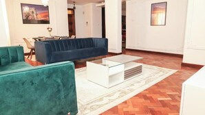 Un salon avec un canapé bleu, une table basse blanche et un tapis à motifs.