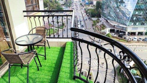 Un balcon doté d’un sol recouvert d’un gazon artificiel vert, de deux fauteuils en osier et d’une table en verre.