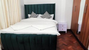 Un lit bien fait, avec une tête de lit verte, une literie blanche et deux coussins décoratifs.