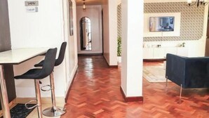 Une cuisine moderne avec un parquet en chevrons, un coin repas comprenant une table et des chaises, et un couloir menant à un placard avec des portes miroir.