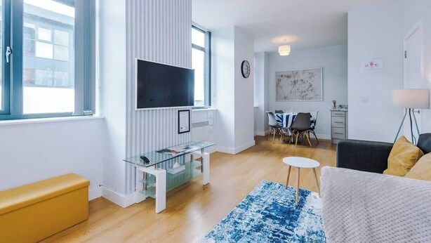 A modern living room with a flat-screen TV, a glass coffee table, a sofa, and a dining area with a table and chairs.