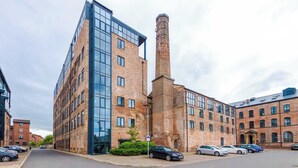 A modern building with a tall chimney, large windows, and a parking lot with cars.