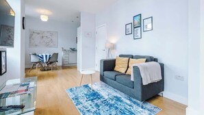 A modern living room with a grey sofa, a blue rug, and a dining area with a table and chairs.