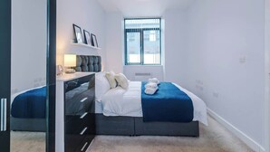A bedroom with a bed, bedside table, lamp, and a window.