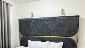 Une chambre à coucher avec un grand lit, une tête de lit grise, une table de chevet blanche et un tapis moelleux.