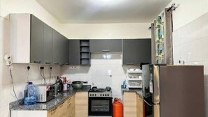 Une cuisine compacte avec des meubles gris, une cuisinière à gaz, un four encastré, un réfrigérateur et un distributeur d’eau.