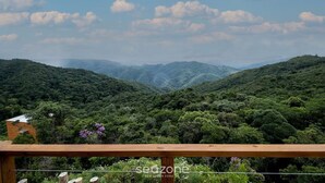 Une vue panoramique d’un paysage montagneux, avec une végétation luxuriante et une rambarde en bois au premier plan.