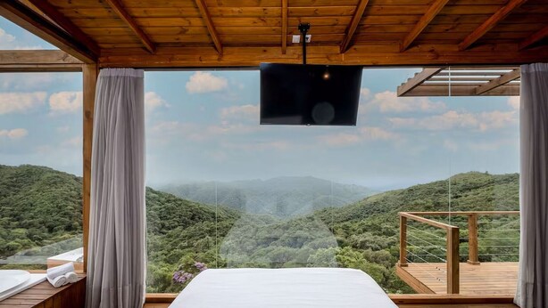Une chambre avec un grand lit, un plafond en bois et un téléviseur fixé au mur.